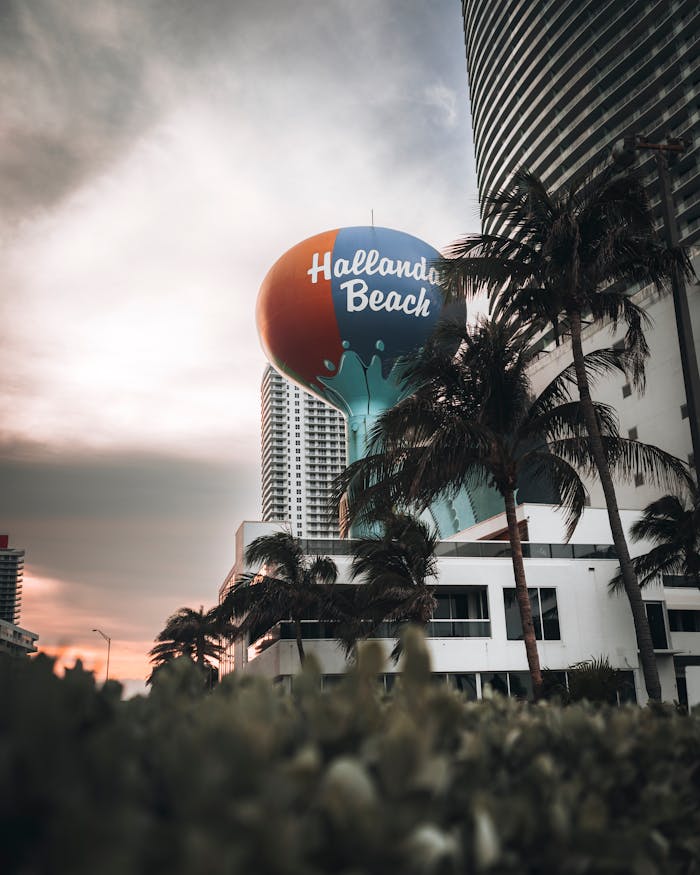 View of Hallandale Beach water tower with palm trees and urban landscape during sunset.